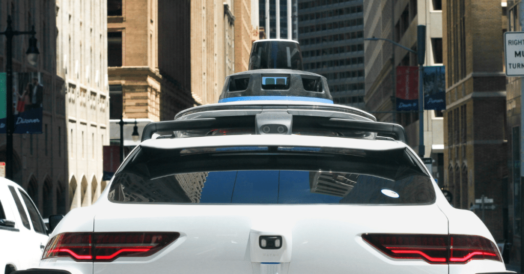 A robotaxi driving through a modern urban environment, surrounded by other road users and city traffic. The vehicle represents autonomous mobility and the growing role of self-driving transport in future mobility systems.